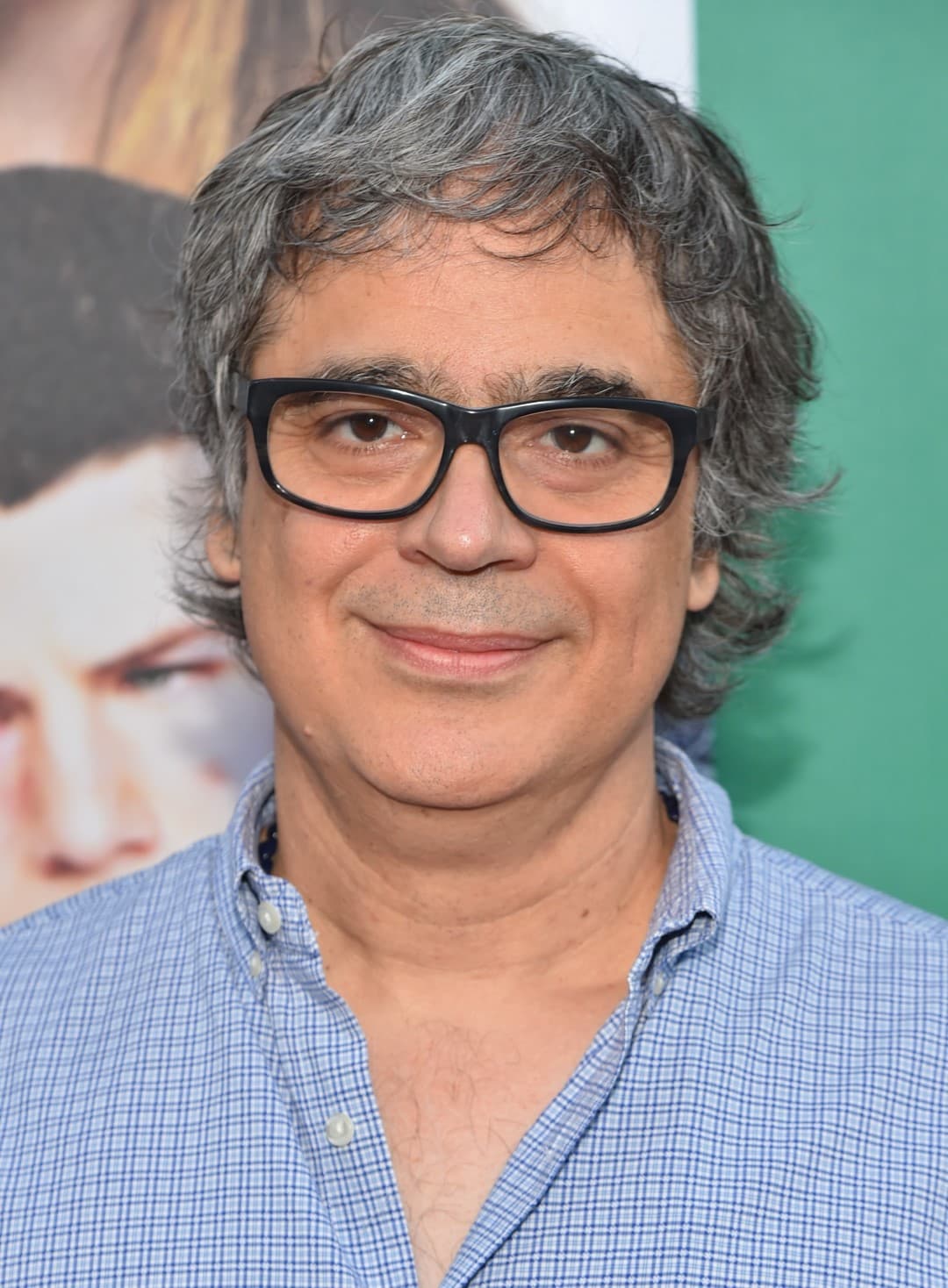 Smiling middle-aged man with wavy salt-and-pepper hair, black-rimmed glasses, and a blue checkered shirt.