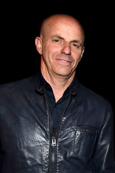 Neal Adams smiling while wearing a dark blue leather jacket against a black background.